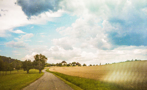 Empty road amidst field against sky