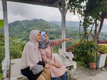Female friends wearing hijabs looking away while sitting on observation point