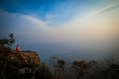 Man sitting on rock against sky