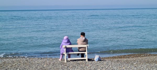 Rear view of men sitting at beach against sky