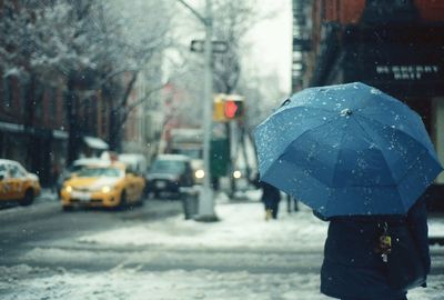 Rear view of person in umbrella on street during snowfall