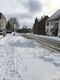 Snow covered street by houses against sky