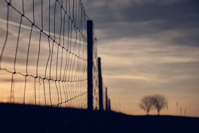 Silhouette fence on field against sky at sunset