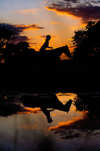 Silhouette men by lake against sky during sunset