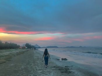 Rear view of man standing on land against sky during sunset