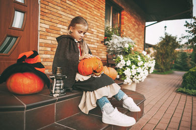 High angle view of girl sitting by pumpkin