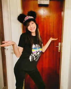 Portrait of smiling young woman standing against door at home