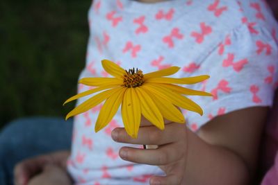 Midsection of child holding sunflower while sitting outdoors