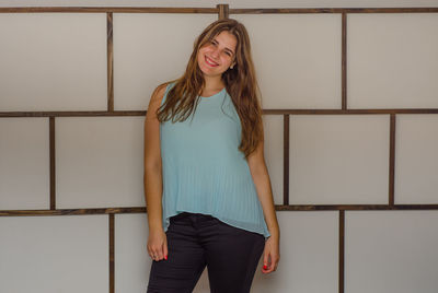 Portrait of happy young woman standing against patterned wall