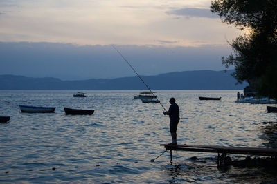 Silhouette man fishing in sea against sky