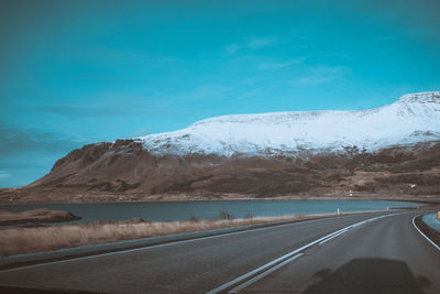 Road by snowcapped mountains against blue sky