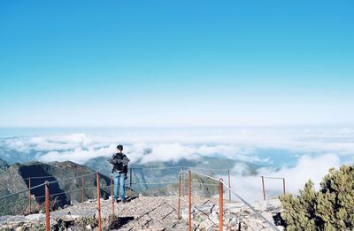 Rear view of man standing by railing looking at view of landscape