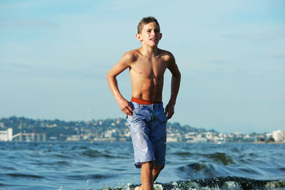 Shirtless boy walking in sea against sky