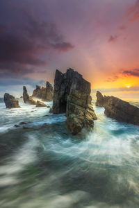 Rocks in sea against sky during sunset