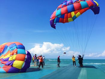 People with colorful parachutes by sea against sky