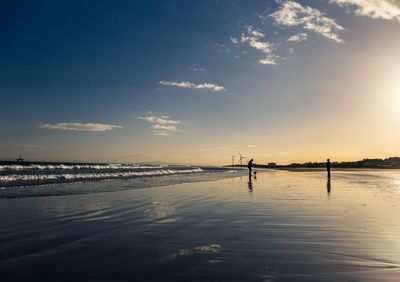 Silhouette people on beach against sky during sunset