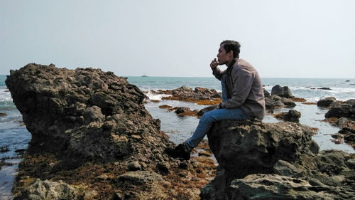 Man standing on rock by sea against clear sky