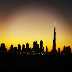 Silhouette burj khalifa amidst buildings against sky at sunset