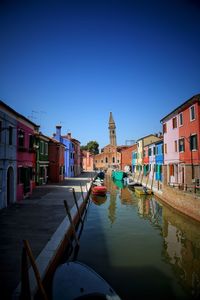 Canal passing through city against clear blue sky