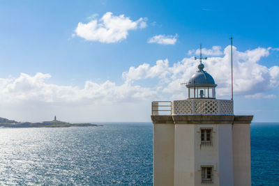 Lighthouse on sea against cloudy sky