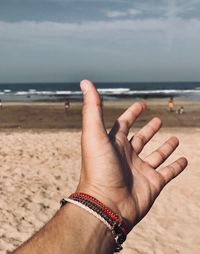 Midsection of person hand on sand at beach against sky