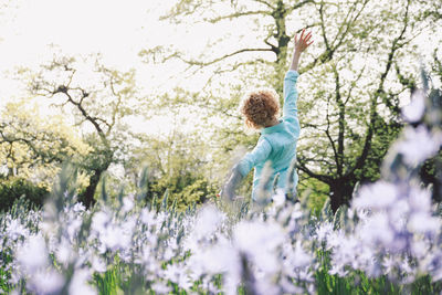 Rear view of woman standing arms outstretched on flowerbed