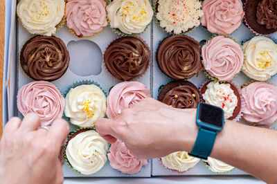 Female hands placing beautifully decorated home baked buttercream cupcakes in carton delivery box.