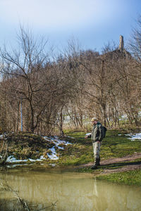 Man standing by bare trees against sky