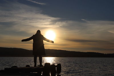 Silhouette man standing on shore against sky during sunset