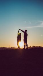 Silhouette people standing on land against sky during sunset