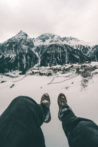 Low section of man sitting on snowcapped mountain against sky
