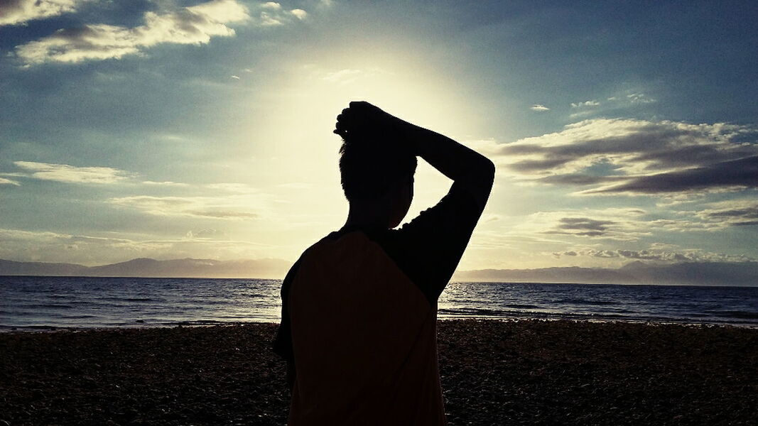 SILHOUETTE MAN STANDING ON BEACH AGAINST SKY