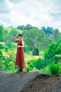 Young woman wearing sunglasses standing on mountain against cloudy sky