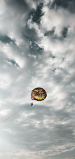 Low angle view of people paragliding against cloudy sky