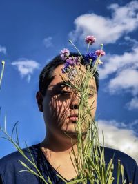 Low angle view of man with cornflowers against cloudy blue sky.