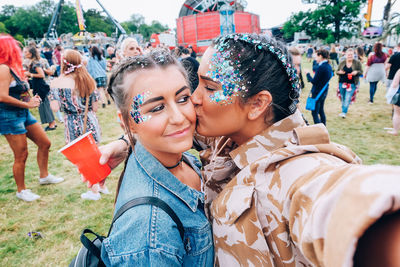 Woman with glitter kissing friend on field