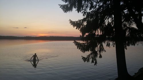 Silhouette man by lake against sky during sunset