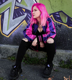 Portrait of young woman sitting on pink wall