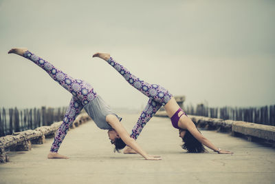 Friends doing yoga on pier against clear sky