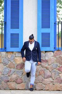 Full length of a young man against closed window on building