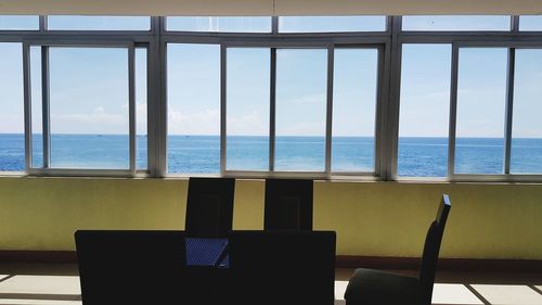 Chairs and table by sea against sky seen through window