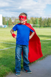 Full length of boy in superman costume standing on road against sky