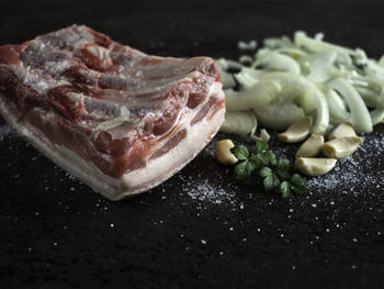 High angle view of rib meat with garlic and herbs against black background