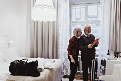 Smiling senior couple reading card while standing in hotel room