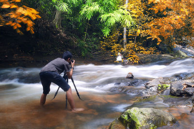 Rear view of man photographing in river at forest