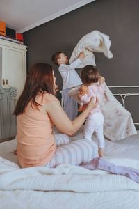 Cheerful mother playing with son and daughter on bed at home