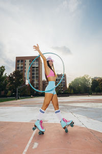 Happy woman practicing roller skating with hoop at sports court