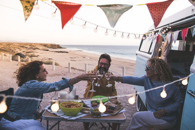 Friends toasting drinks while sitting at beach