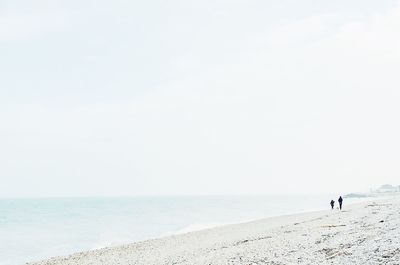 People walking on beach against clear sky