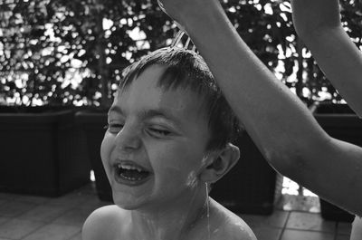 Close-up of happy wet boy by cropped sister hands